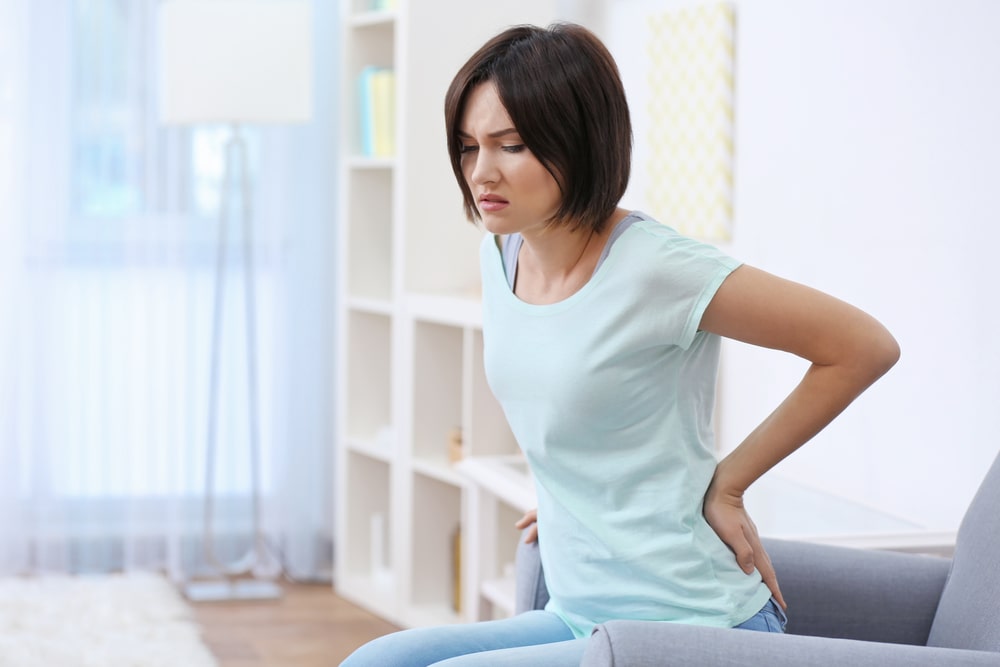 woman sitting on couch holding her back who needs chiropractic treatment for back pain